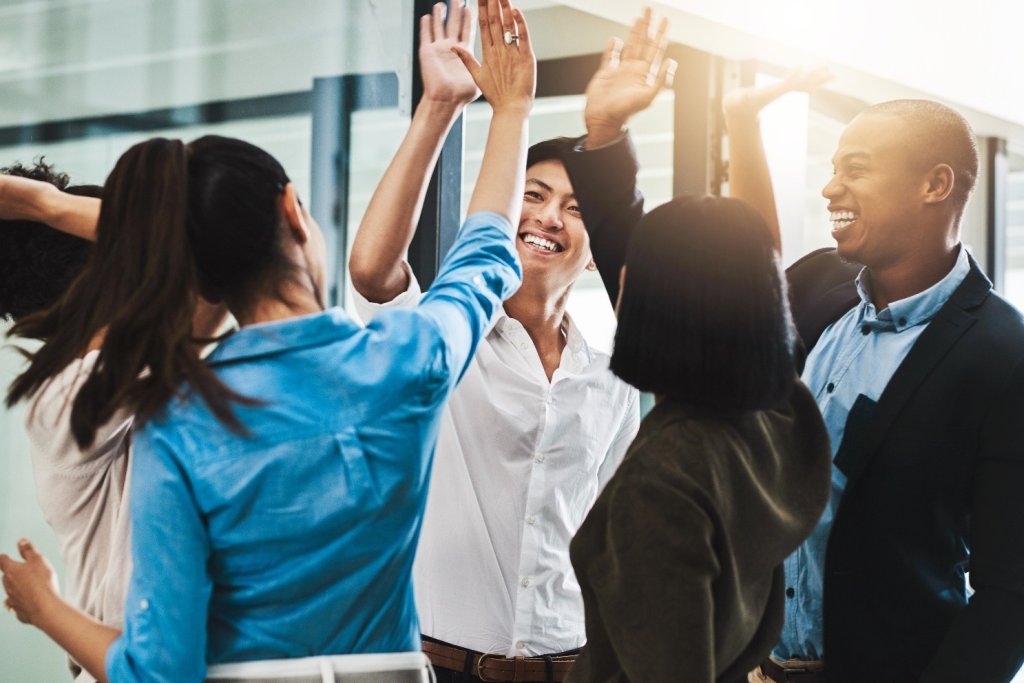 Fünf Mitarbeiterinnen und Mitarbeiter, die im Kreis stehen, lachen und sich High-Five geben.