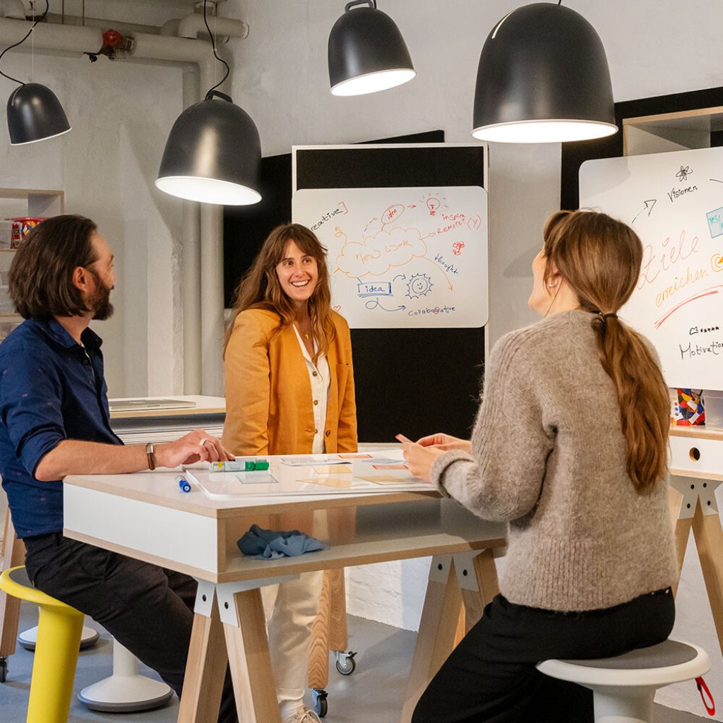 Dynamisch und flexibel: drei Mitarbeitende arbeiten in einem kreativen Meetingraum, um ihre Ideen und Ziele auszutauschen. MYWORKSPACE by Lyreco unterstützt bei der Gestaltung eines kreativen und flexiblen Arbeitsplatzes, um die die Produktivität zu steigern.